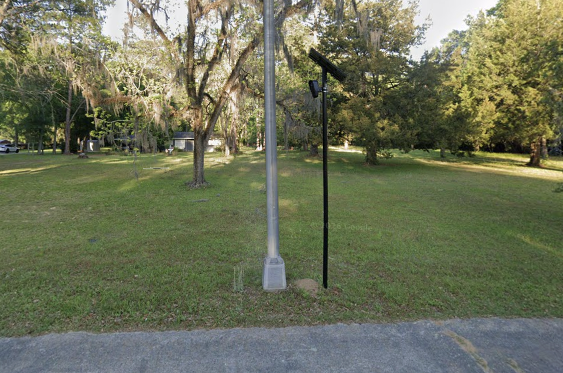 Flock camera on a pole at 2416 Radium Springs Rd, on open mowed lawn with no brush nearby